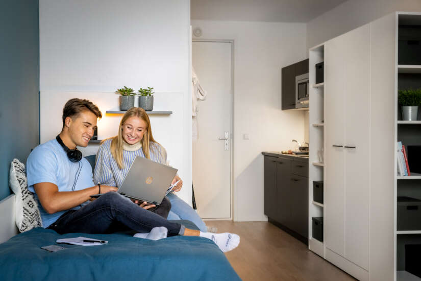 a couple sitting on a bed looking at a laptop